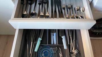 Uma gaveta com utensílios de cozinha bem organizados, incluindo colheres, garfos, facas e um prato azul.
