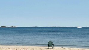 Ein Strand mit einem einzelnen grünen Stuhl und einem entfernten Boot.