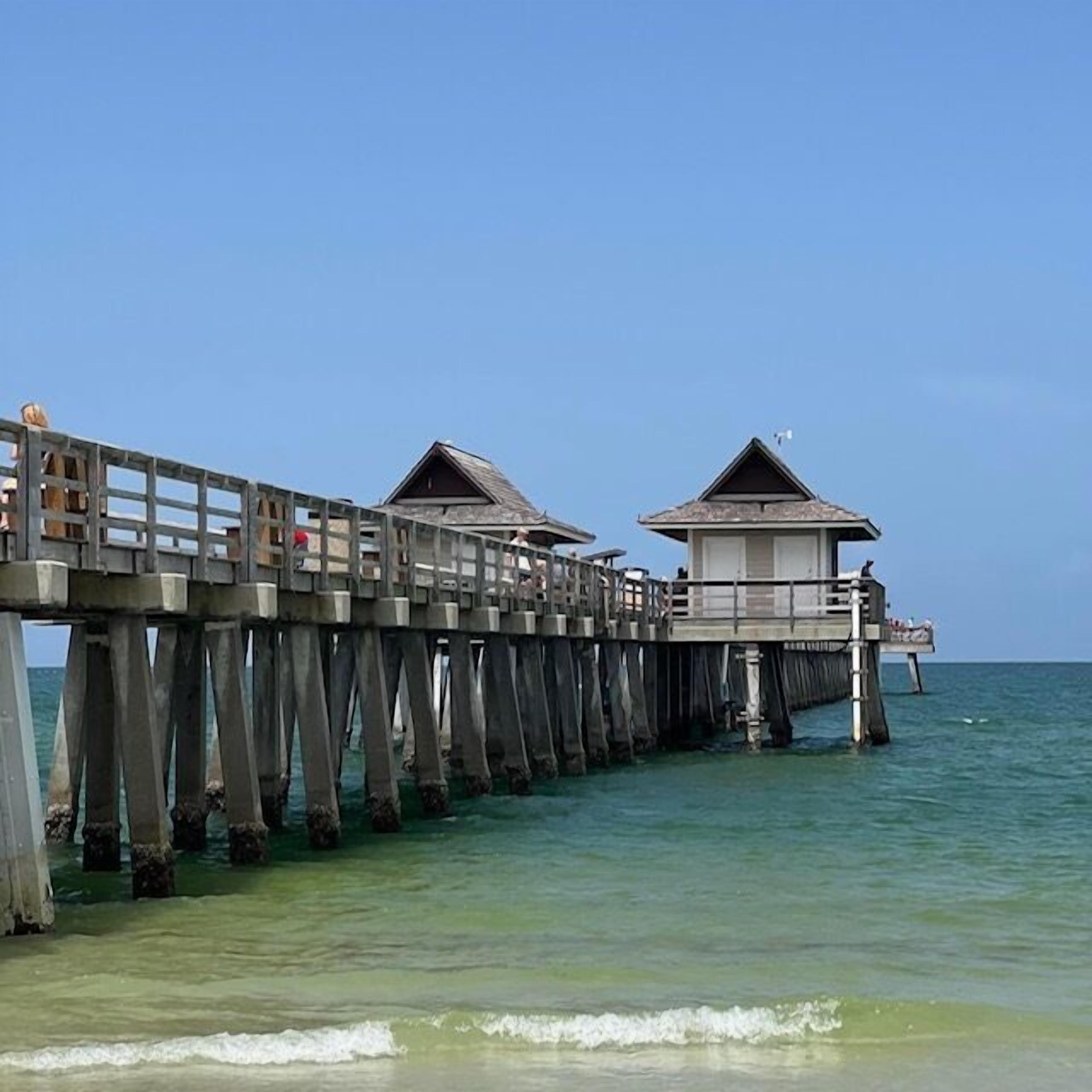 A wooden pier with two small structures at the end, extending into calm waters.
