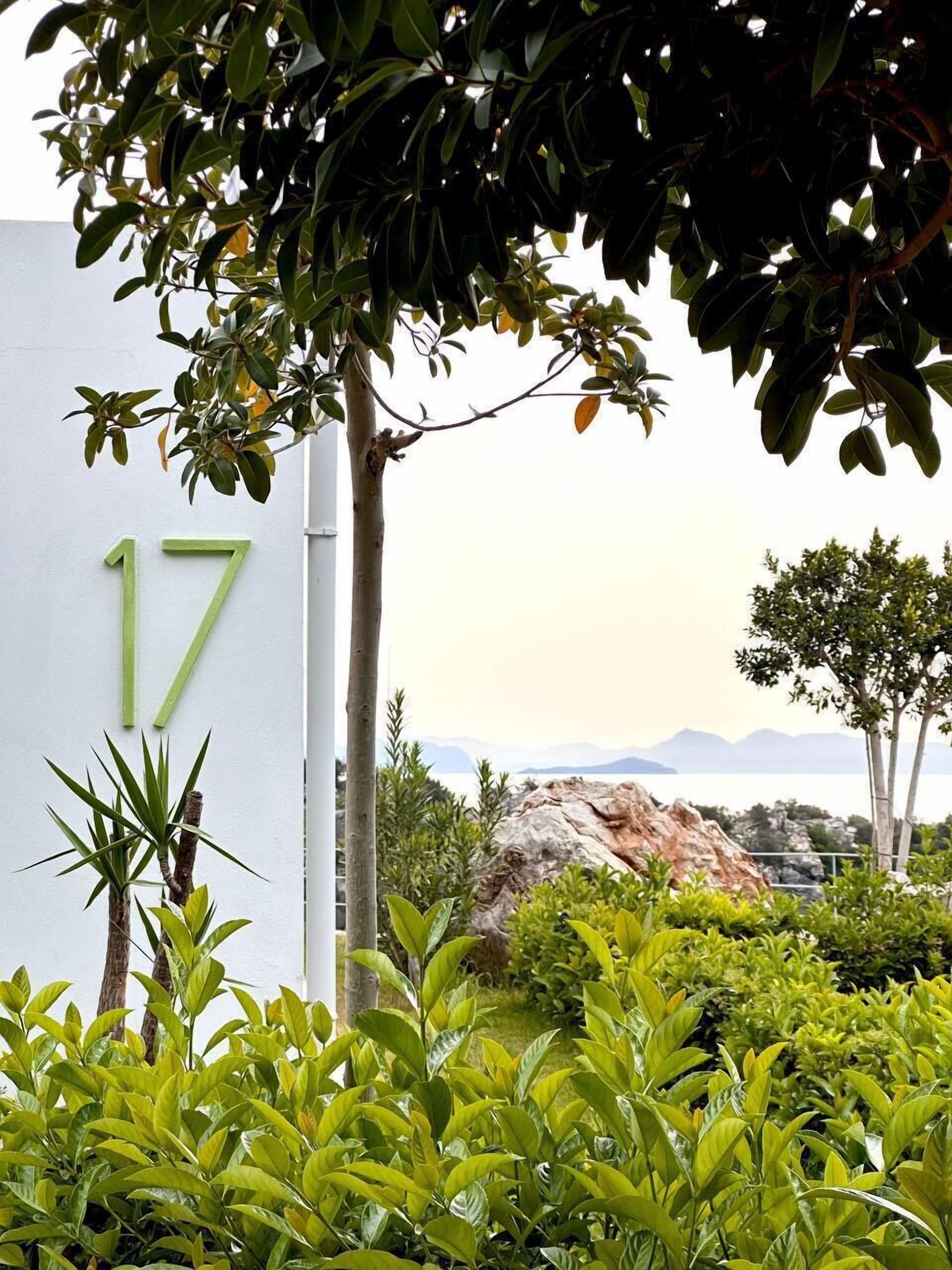 Un bâtiment portant le numéro 17, entouré d’une végétation luxuriante et offrant une vue sur la mer et les montagnes.