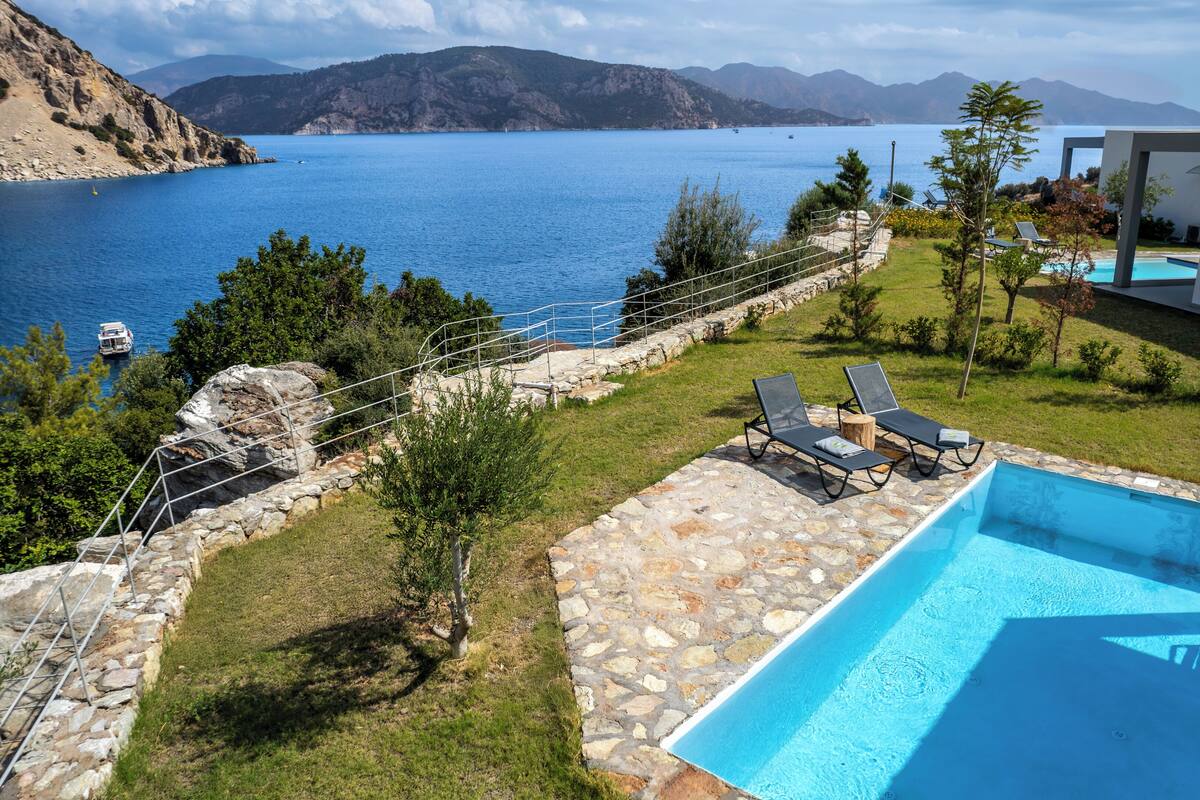 A pool area with a view of the sea, stone steps, and a modern building.