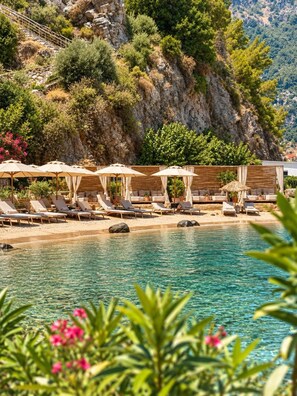 A pool area with lounge chairs and umbrellas, surrounded by greenery and a rocky cliff. - Z-Villas (Marmaris)