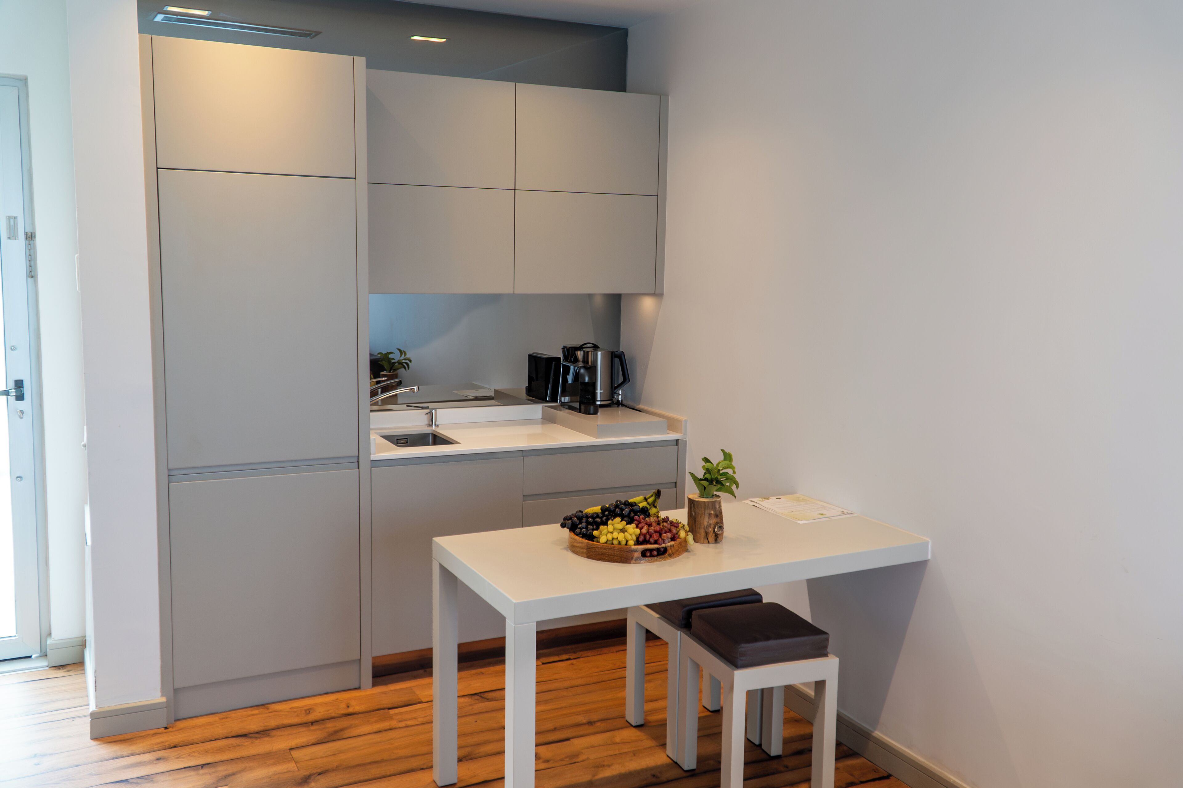 Una cocina compacta con encimera blanca, cafetera y frutero.