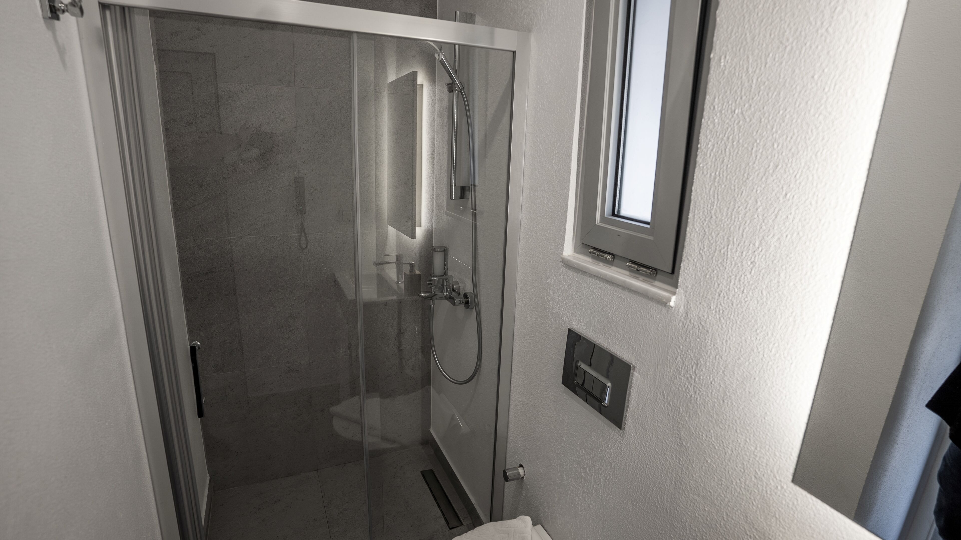 Une salle de bain moderne avec une douche à parois de verre, une petite fenêtre et un porte-serviettes.