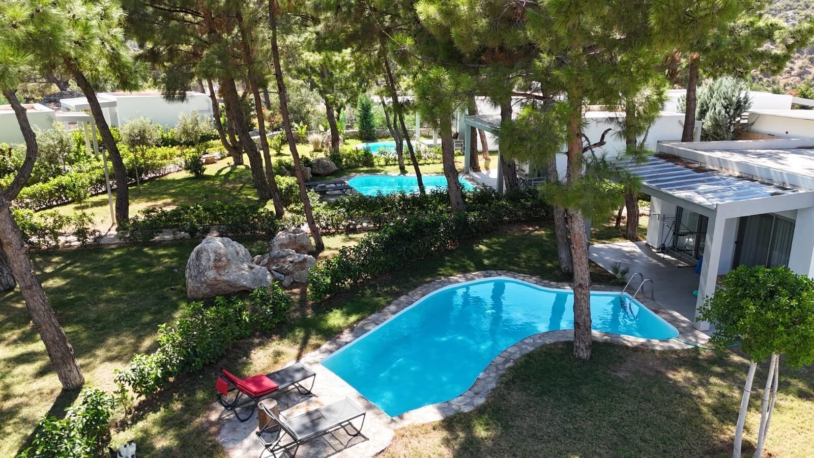 A swimming pool surrounded by trees and rocks, with a small deck and lounge chairs.