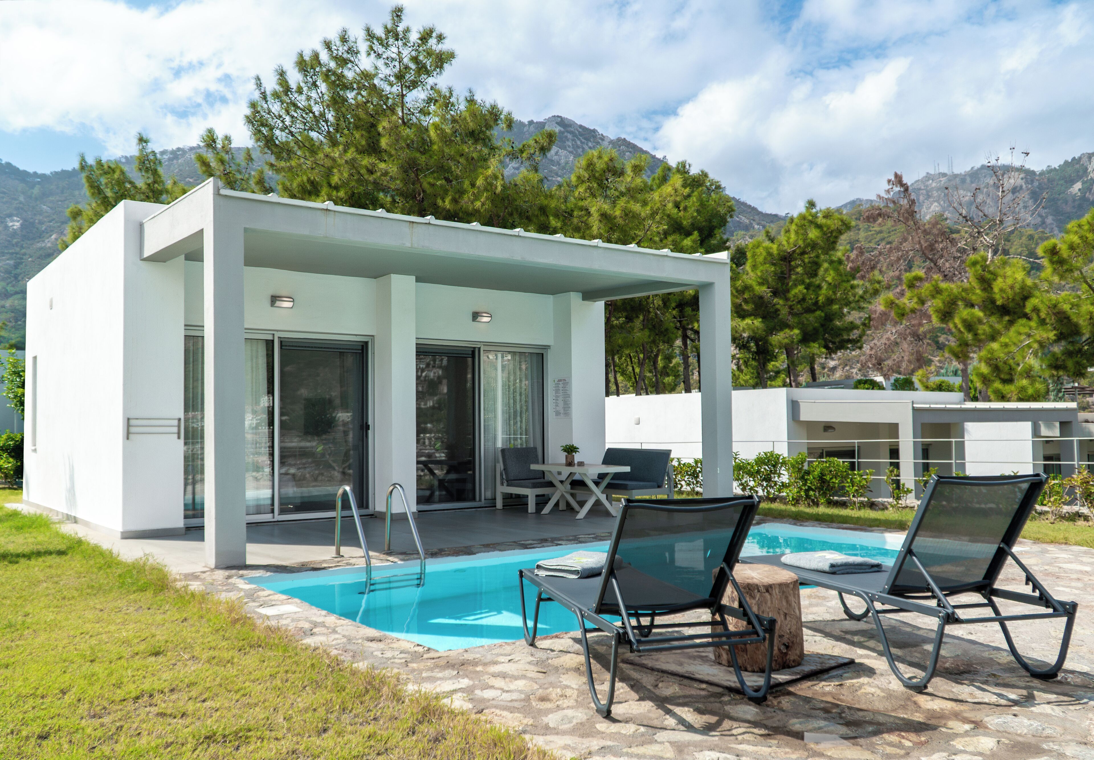 A modern outdoor pool area with lounge chairs, a wooden table, and a covered seating area.