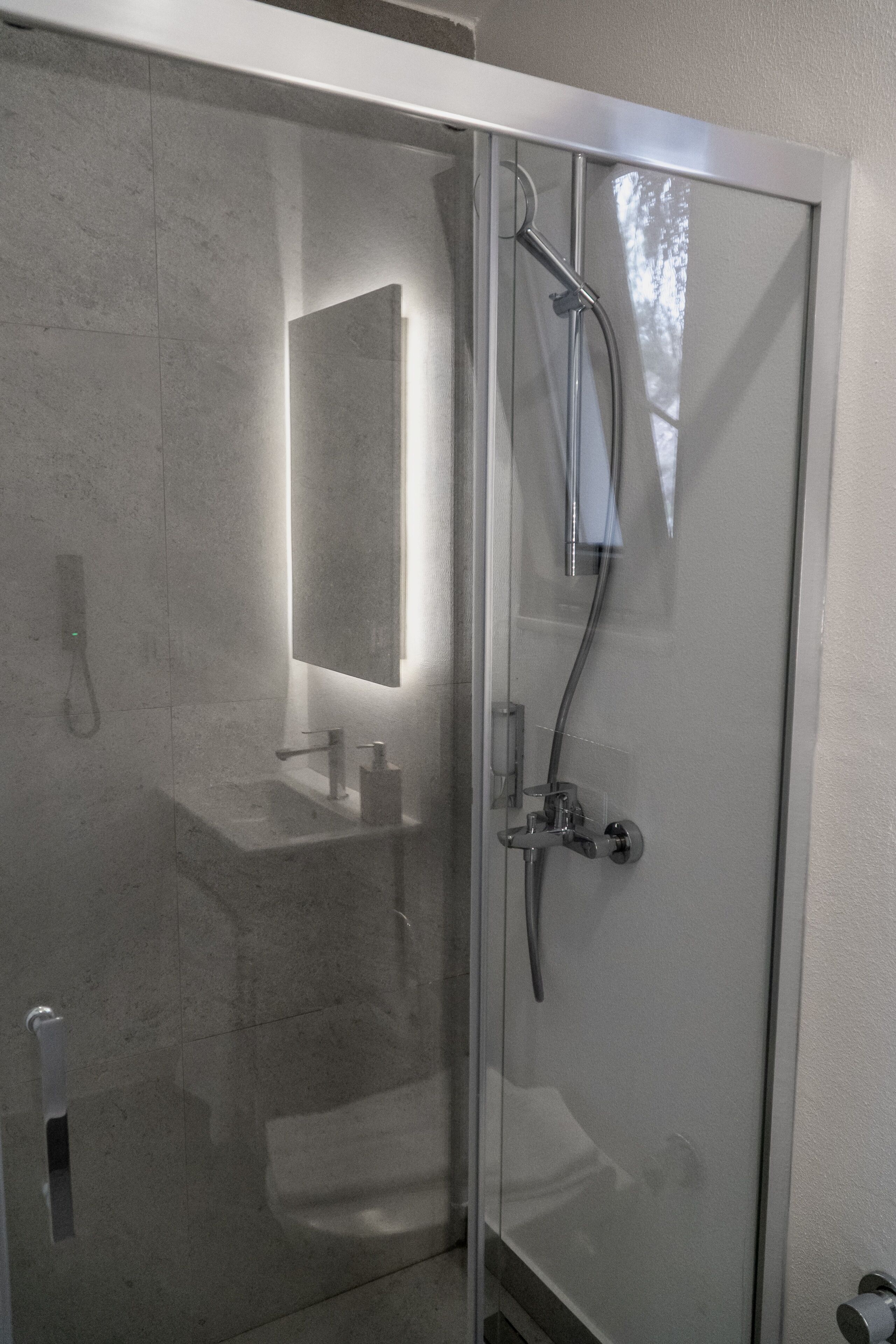 Un baño moderno con cabina de ducha de vidrio, lavamanos a la vista y un espejo.