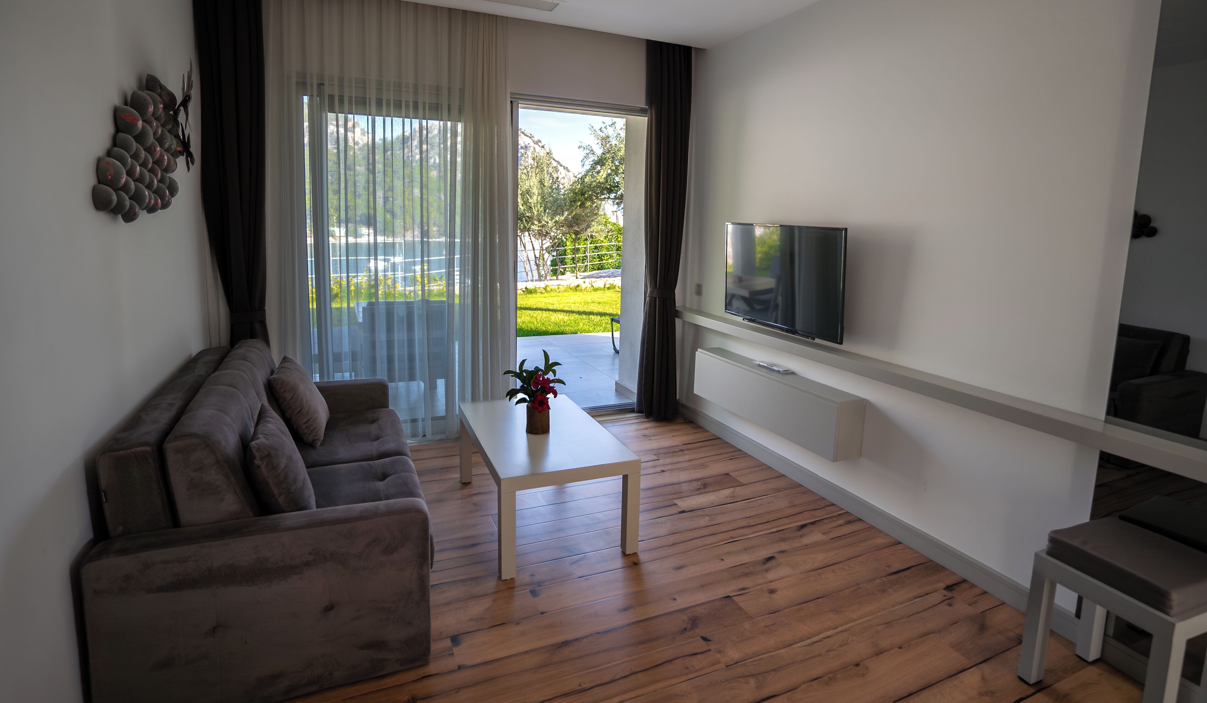 A modern living room with a sofa, a coffee table, a TV mounted on the wall, and a sliding glass door leading to a balcony.