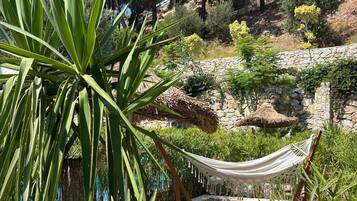 A hammock in a lush garden with a stone wall and a rocky hillside in the background.