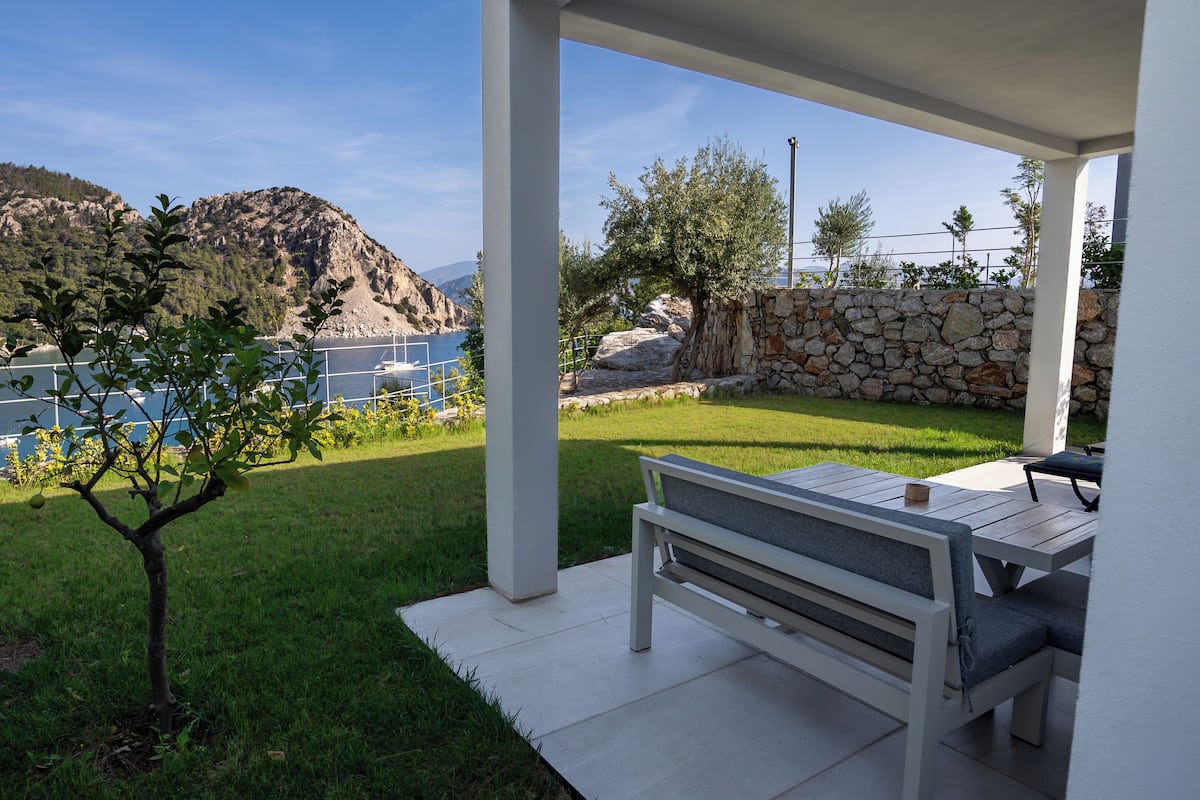 A patio with a table and bench, overlooking a grassy yard and a stone wall.