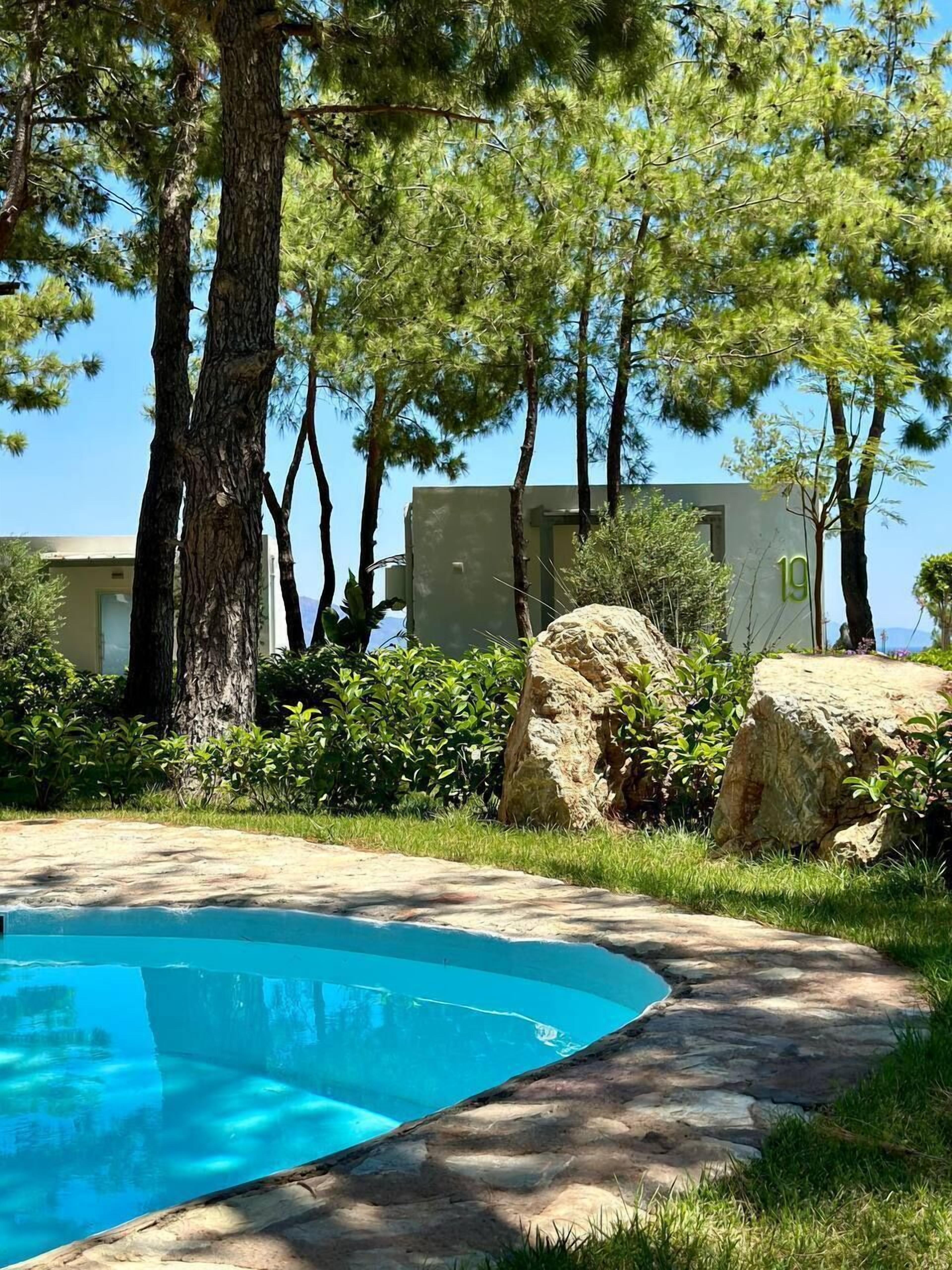 Una piscina con un sendero de piedra, rodeada de árboles y un edificio donde se ve el número 19.