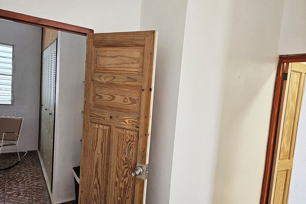 A wooden door with a metal handle, a chair, and a window with blinds in the background.