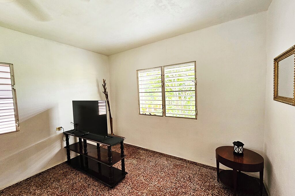 A room with a television on a stand, a small table with a decorative item, and a window with blinds.