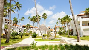 A resort with multiple white buildings, palm trees, and a central thatched structure. - Just  few steps from Beach, Enjoy a Sunrise in this Wonderful place (Punta Cana)