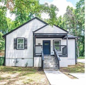 Stroll up to the charming front porch, featuring a dark blue door and shutters, and a black railing.