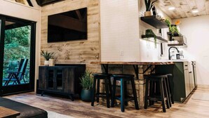 A modern kitchen with a wooden ceiling, a large window, and a bar area with stools. - The Treehouse @Brandywine Grove (Sugarcreek)