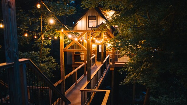 A wooden treehouse with a wooden staircase and string lights. - The Treehouse @Brandywine Grove (Sugarcreek)