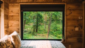A wooden cabin with a large window offering a view of a forest. - The Treehouse @Brandywine Grove (Sugarcreek)