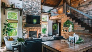 Una sala de estar acogedora con chimenea de piedra, un televisor grande y una escalera de madera.
