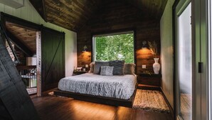 Un dormitorio con cama, ventana, lámpara y techo de madera.
