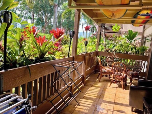 A covered outdoor area with a wooden deck, chairs, and potted plants.