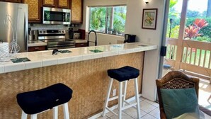 A kitchen with a large island, stainless steel appliances, and a view of greenery outside.