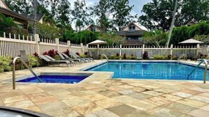 A swimming pool with two separate sections, surrounded by a white fence and lounge chairs.