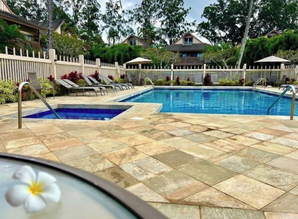 A swimming pool with two separate sections, surrounded by a white fence and lounge chairs.