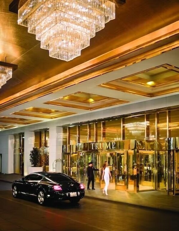 A hotel entrance with a grand chandelier, a glass facade, and a sign reading "TRUMP".