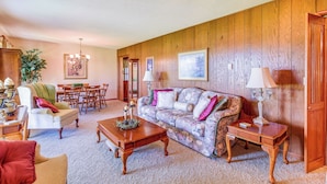 A cozy living room with a floral sofa, wooden coffee table, and a dining area with wooden chairs and a table.