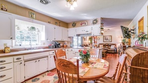 A spacious kitchen with white cabinetry, a dining area with a wooden table and chairs, and a living room with a sofa and a piano.