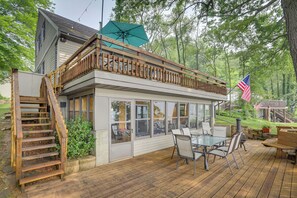 A covered deck with a glass enclosure, wooden railing, and outdoor furniture. - Lakefront Sister Lakes Vacation Rental w/ Dock! (Dowagiac)
