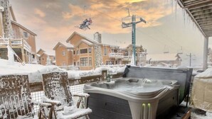 A hot tub in a snowy outdoor setting with a view of a ski lift and buildings in the background.