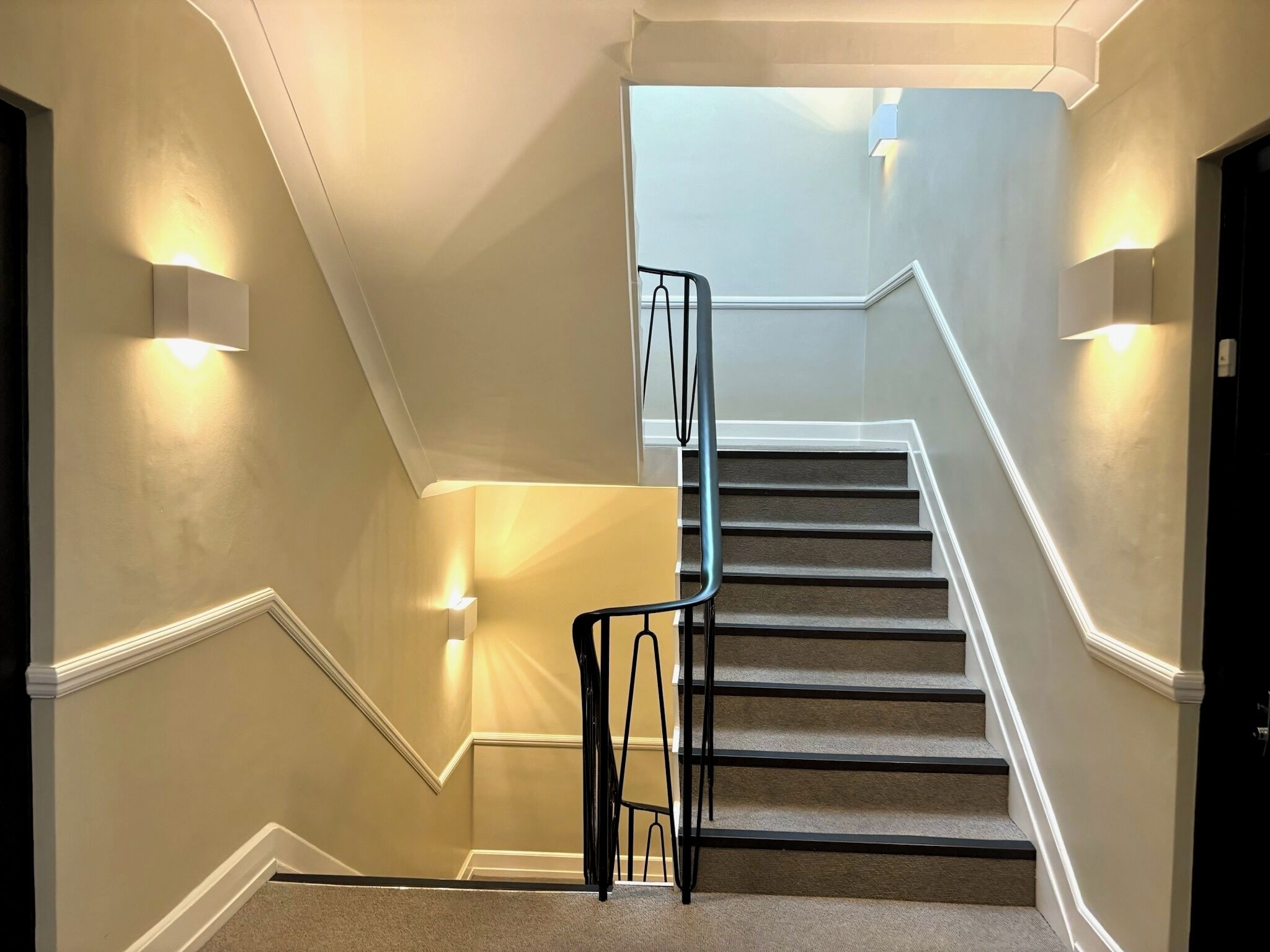 A staircase with a handrail, carpeted steps, and wall-mounted lighting.