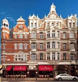 Un edificio histórico de varias plantas, con una combinación de fachadas de ladrillo rojo y piedra blanca, y ventanas grandes.