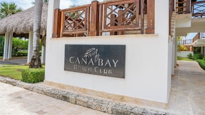 Letrero de Canabay Beach Club, con una palmera y una estructura de techo de paja al fondo.