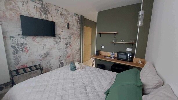 Ein kleiner, einfach eingerichteter Raum mit einem Bett, einem an der Wand montierten Fernseher, einer Mikrowelle auf einem Regal und einer Tür zu einem anderen Raum.