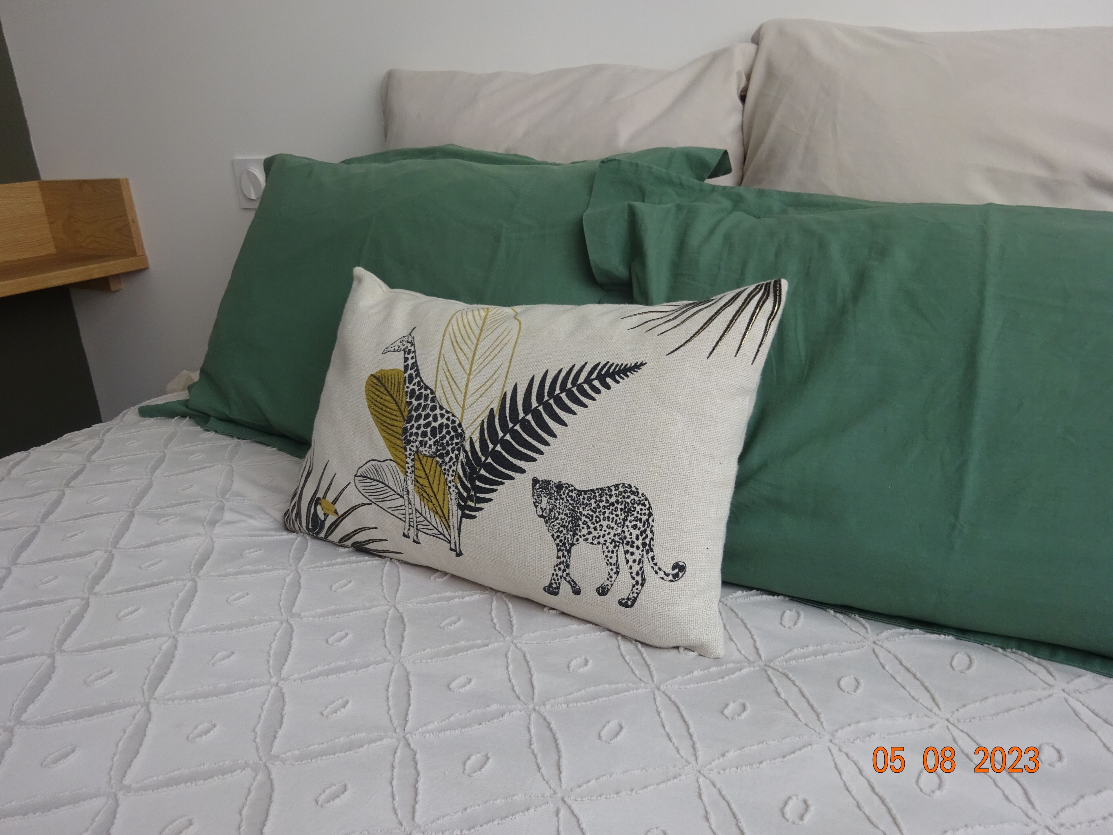 Ein Bett mit einer gesteppten weißen Matratze, grünen Kissen und einem Zierkissen mit Tiermotiven und Blättern.