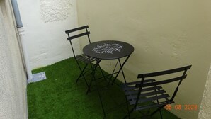 Ein kleiner Außenbereich mit einem runden Tisch und zwei Stühlen, umgeben von einer weißen Mauer und einem Bereich mit künstlichem Rasen.