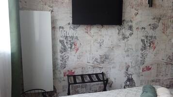 Een slaapkamer met een bed, een bankje, een kledingkast en een aan de muur bevestigde televisie.