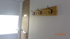 Eine Holztür mit einem Metallgriff und einem kleinen Fenster. An der Wand befindet sich eine Holztafel mit drei schwarzen Haken.