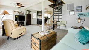 A living room with a beige recliner, a wooden chest, a teal sofa, and a staircase.