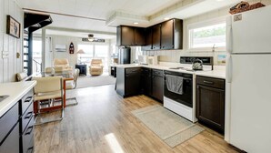 A modern kitchen with dark cabinets, a white refrigerator, and a dining area with a glass table and leather chairs.
