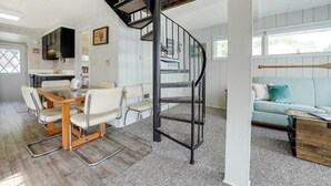 A spacious living area with a dining table and chairs, a black spiral staircase, and a light blue sofa.