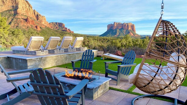 An outdoor patio with lounge chairs, a hanging chair, and a fire pit. - Hiker's Paradise infinity pool, trail access to Chapel of Holy Cross and Mystic (Sedona)