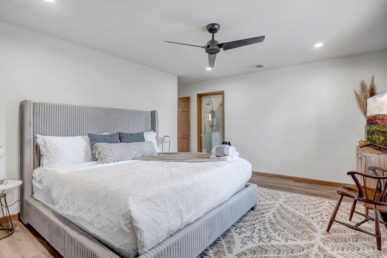 Un dormitorio amplio con una cama grande, un ventilador de techo y una puerta de madera al fondo.