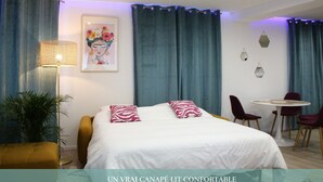 A hotel room with a bed, a desk, chairs, a lamp, and a plant.