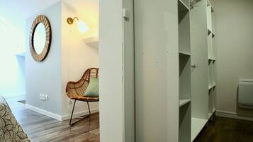 Een kamer met een rieten stoel, een spiegel aan de muur en een witte garderobe met planken.
