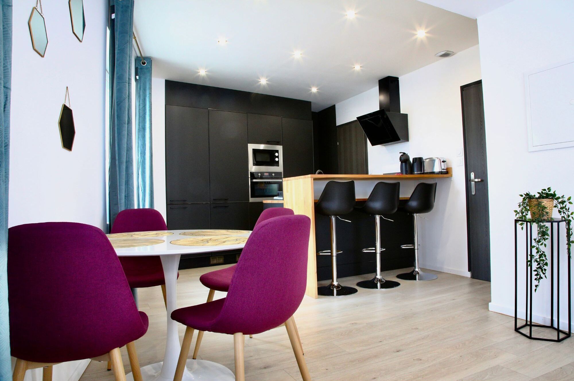 Een moderne keuken met een eethoek, met een ronde tafel en stoelen, een bar met krukken, en een zwarte televisie aan de muur.