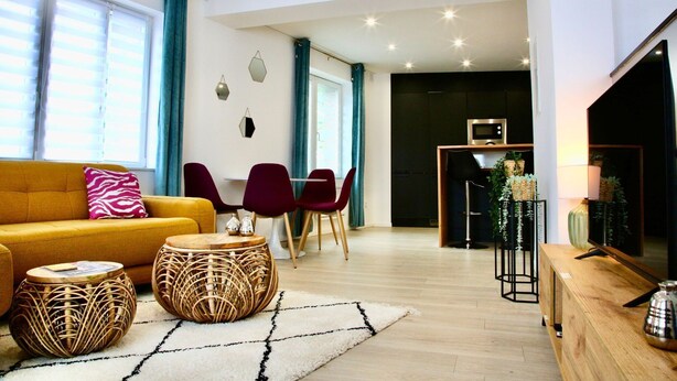 A modern living room with a sofa, two red chairs, a round coffee table, and a TV on a wooden stand.